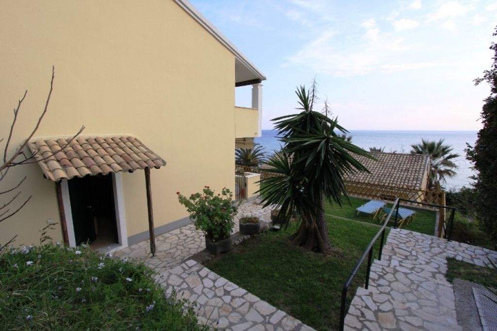 A building with a tiled roof, a stone pathway, and a view of the sea.