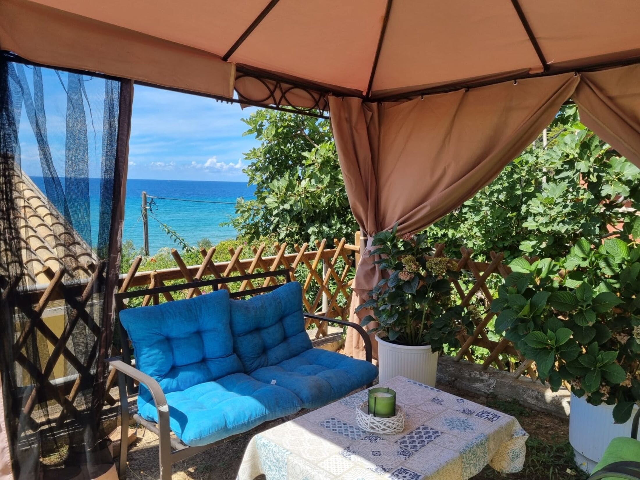 A cozy outdoor seating area with a cushioned chair and a table, overlooking a scenic view of the sea.
