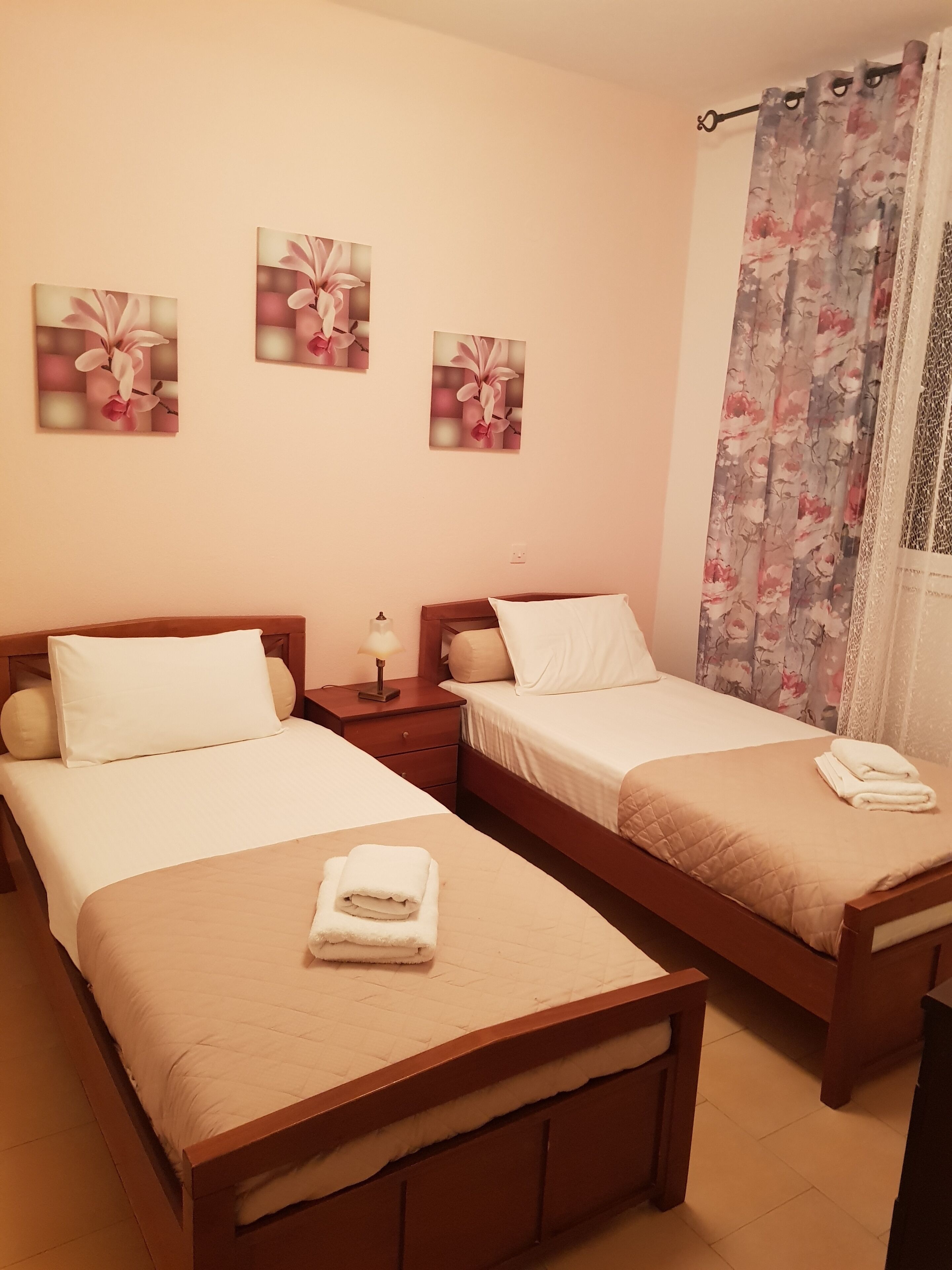 Une chambre d’hôtel avec deux lits simples, une table de chevet avec une lampe et des œuvres d’art florales accrochées au mur.