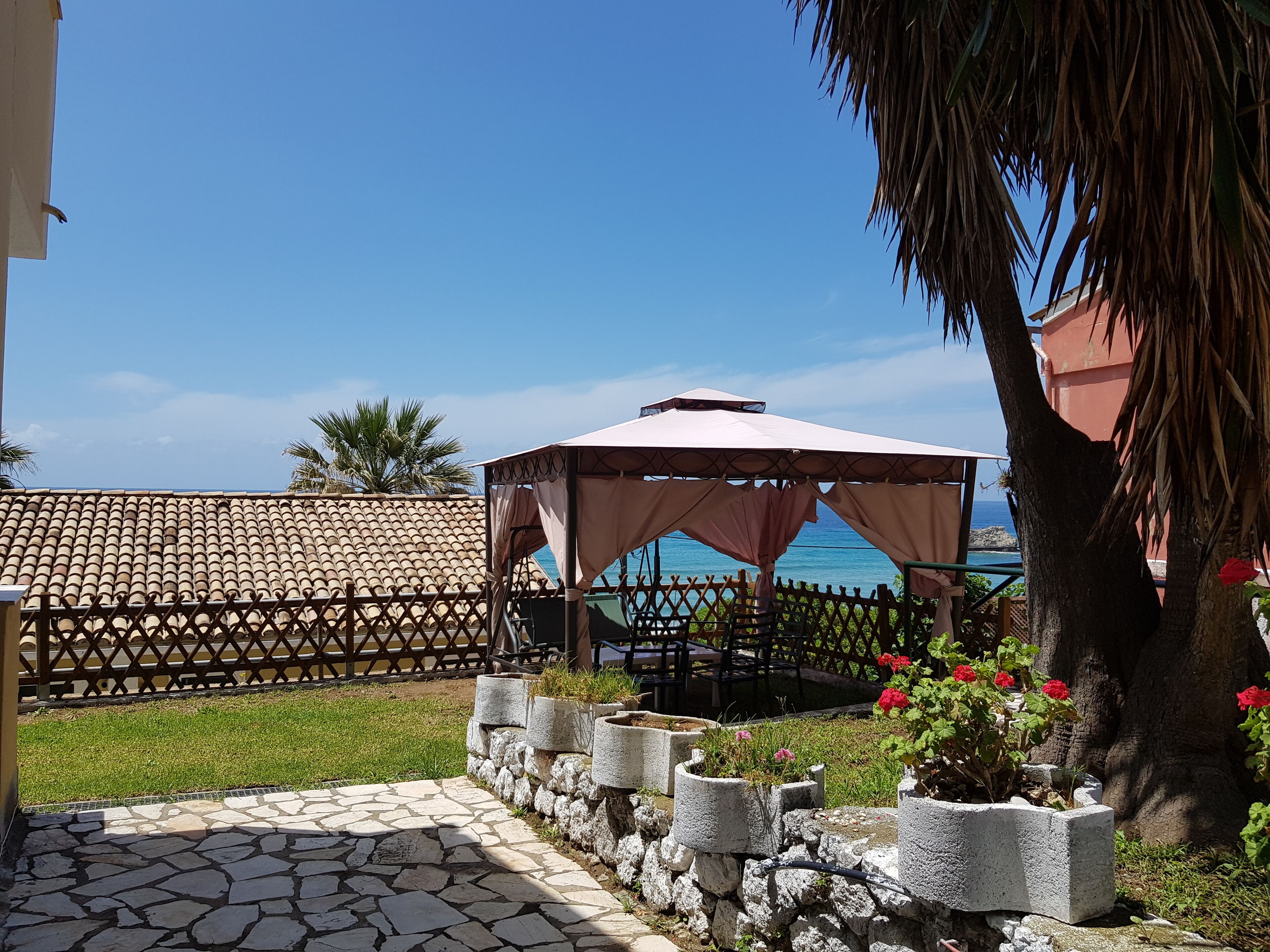 A patio area with a stone floor, a covered seating area, and a view of the sea.