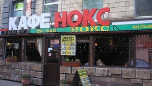 A cafe named "KAΦE HOKC" with outdoor seating and a signboard displaying prices in multiple currencies. - Yourhostel La Femme (Kyiv)