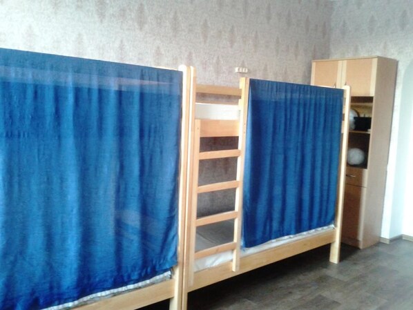 Two bunk beds with blue curtains, a wooden ladder, and a wardrobe in a room with a grey wall and wooden flooring.