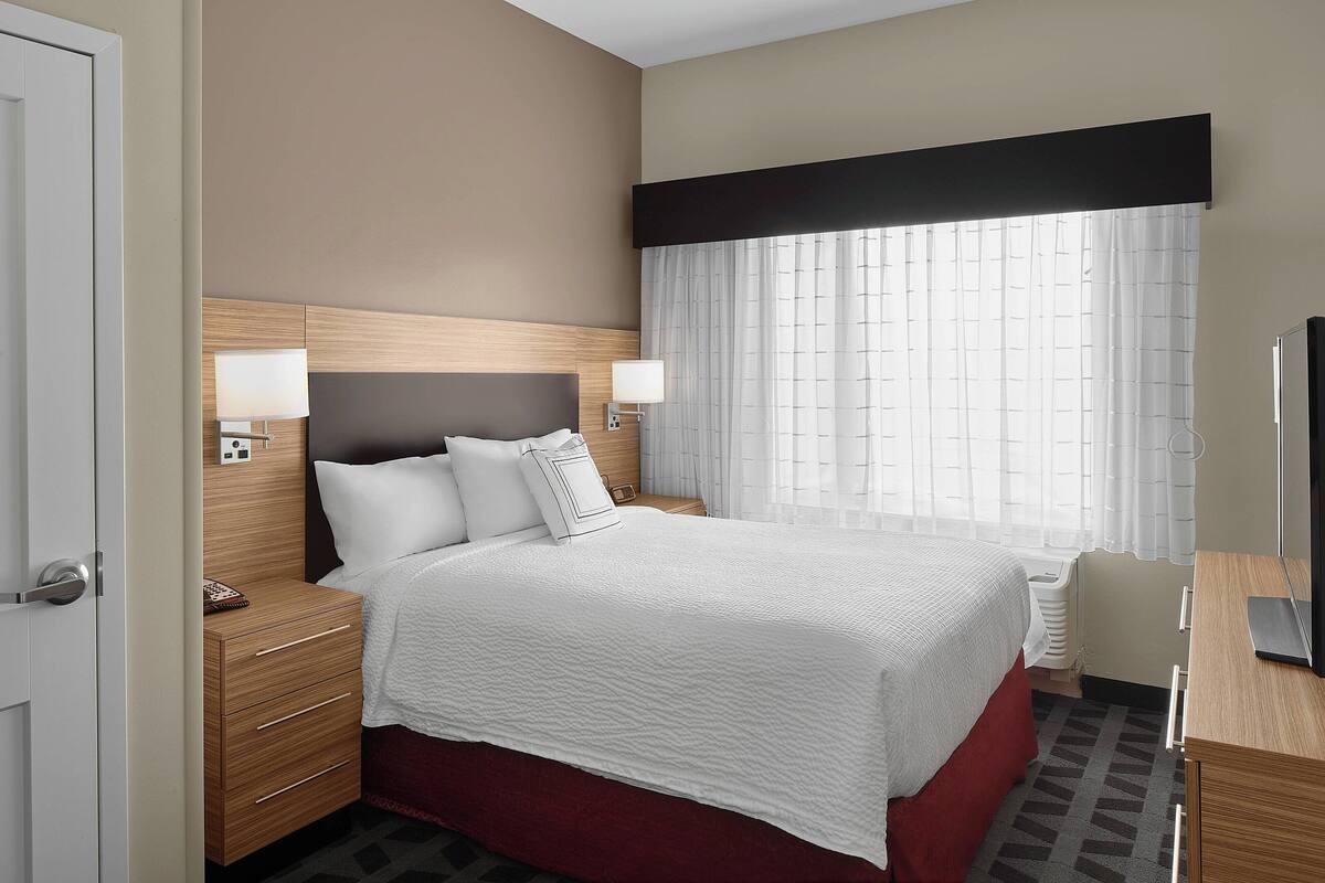 Una habitación de hotel con cama, mesitas de noche, escritorio y televisor.