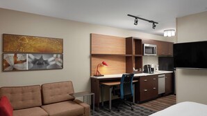 Habitació d'hotel amb sofà, escriptori amb cadira, microones, nevera i televisió de pantalla plana.