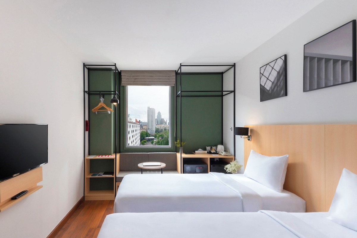 Een hotelkamer met twee bedden, een televisie, een bureau en een raam met uitzicht op de stad.