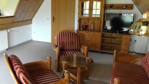 A cozy living room with a sloped ceiling, wooden furniture, a television, and a cabinet. - Apartment above - Landhaus Ulrich (Bergen auf Rügen)