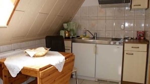 A small kitchen with a wooden table, a chair, a sink, and a stove. - Apartment above - Landhaus Ulrich (Bergen auf Rügen)