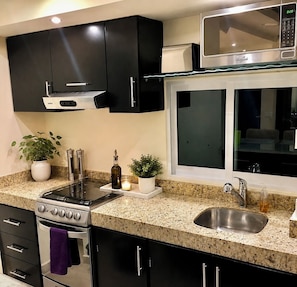 A kitchen with a stove, microwave, sink, and black cabinets.