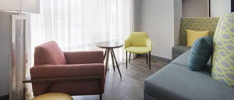 Una habitación de hotel moderna con un sillón rojo, un sillón amarillo y un sofá gris con cojines estampados.