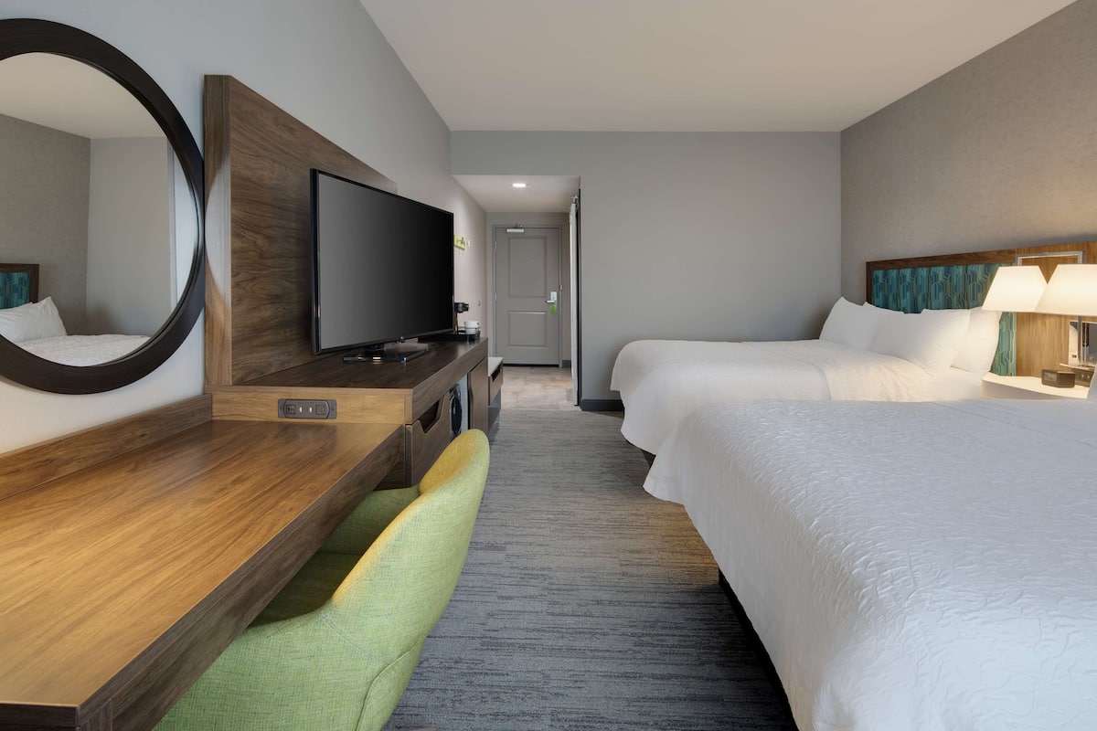 A hotel room with a bed, a desk with a TV, a chair, and a mirror.