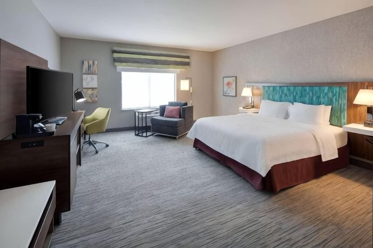 Una habitación de hotel con cama, escritorio, televisor, silla y ventana.