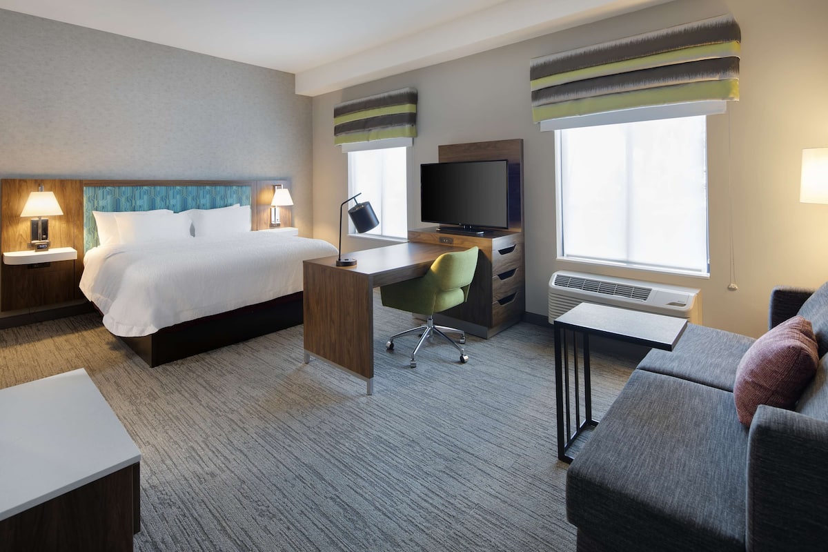 A hotel room with a bed, desk, chair, TV, and a sofa.