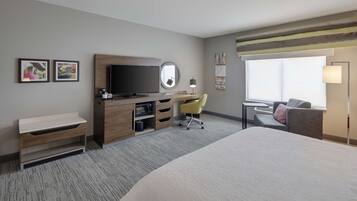 Een hotelkamer met een bed, een bureau met televisie, een stoel, een klein tafeltje en een raam.