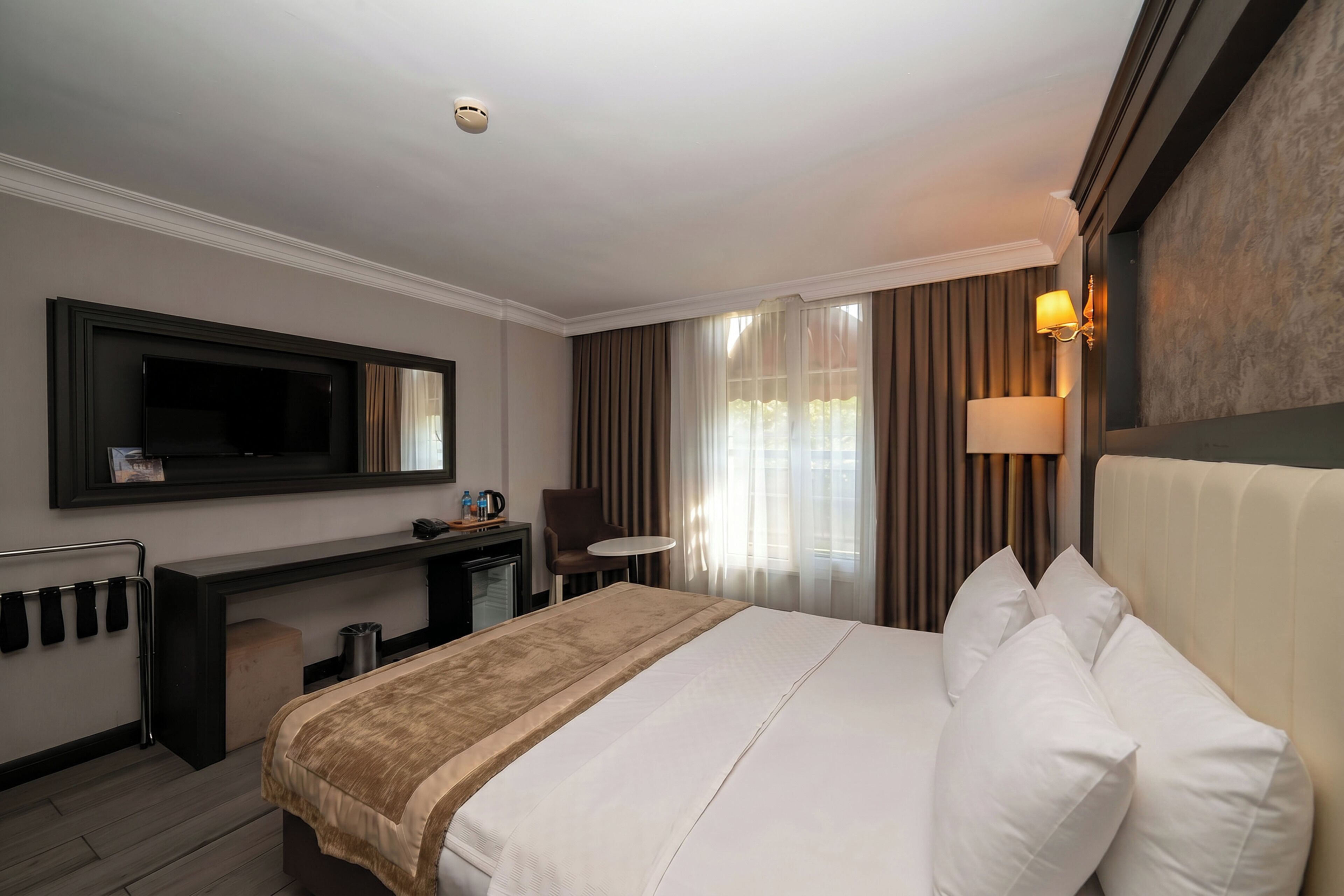 A hotel room with a bed, a desk, a chair, a television, and a lamp.