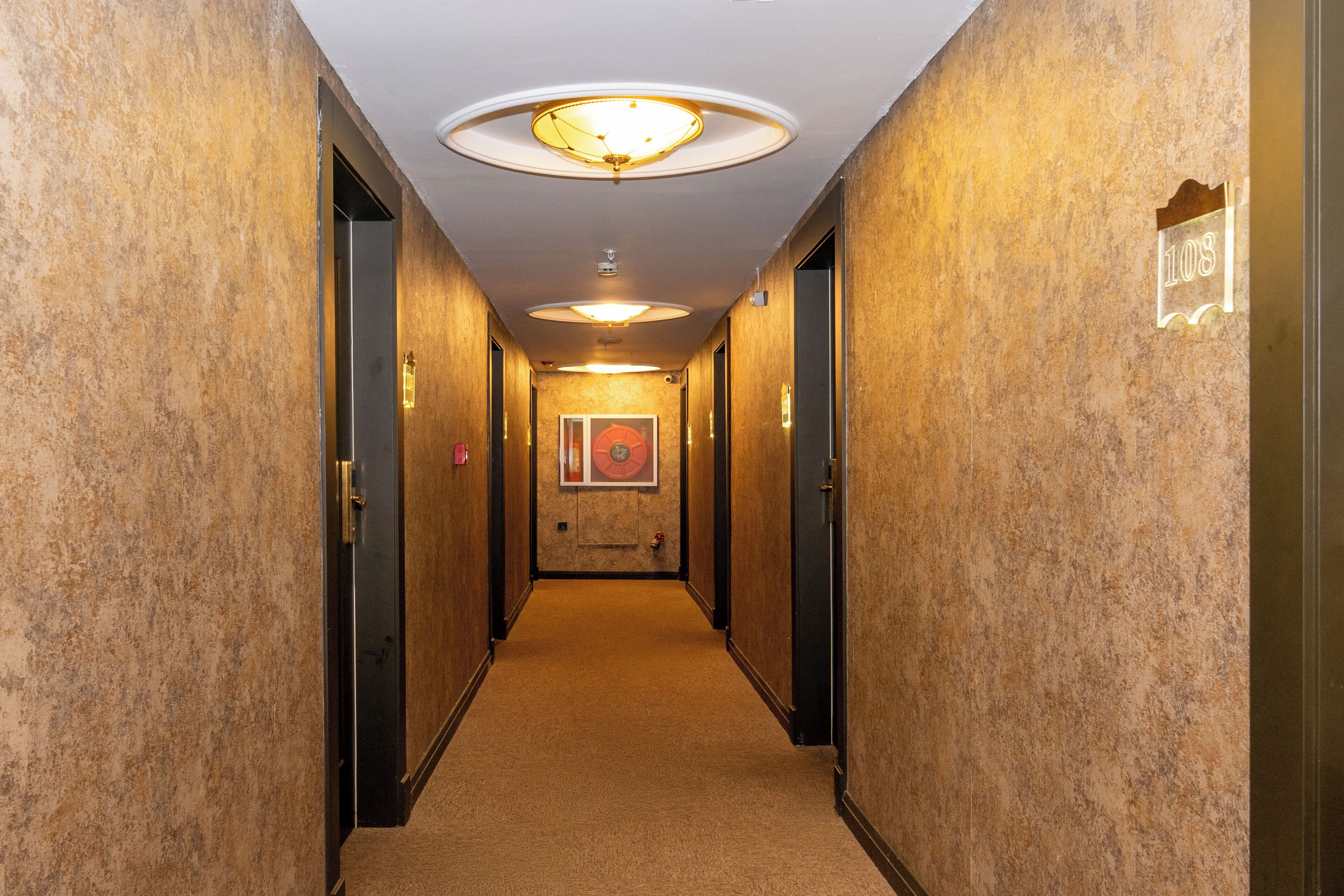 Un pasillo de hotel con pared de mármol, una obra de arte enmarcada y un cartel que indica la habitación 108.