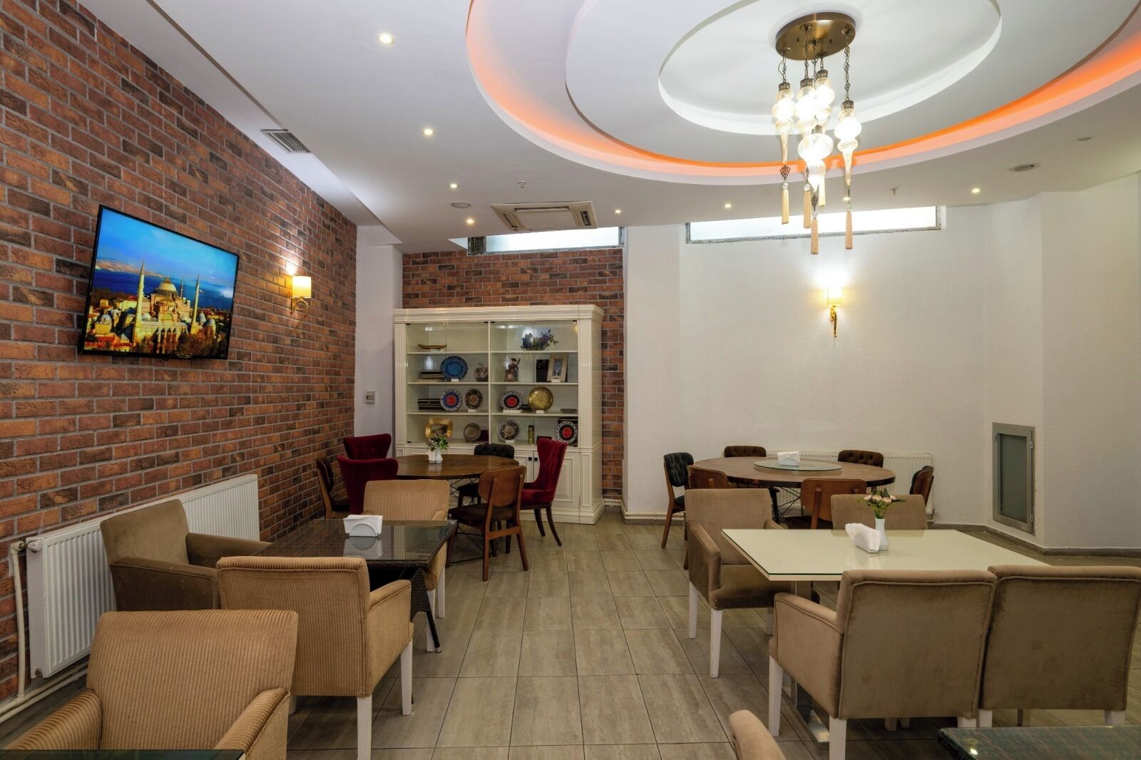 A restaurant with brick walls, a TV, a chandelier, and a dining area with chairs and tables.