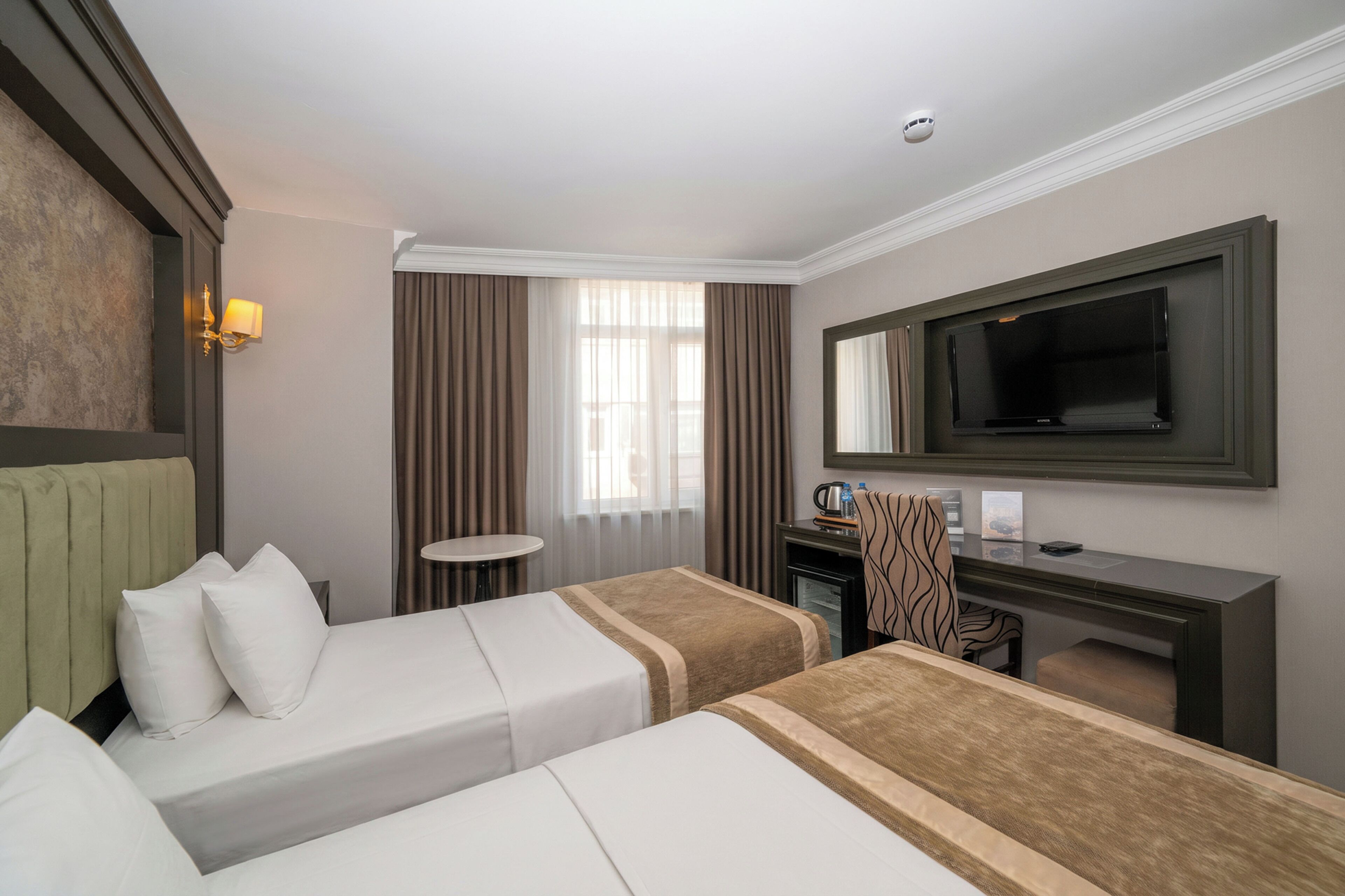 Habitación de hotel con dos camas, un escritorio, un televisor y una ventana con cortinas.