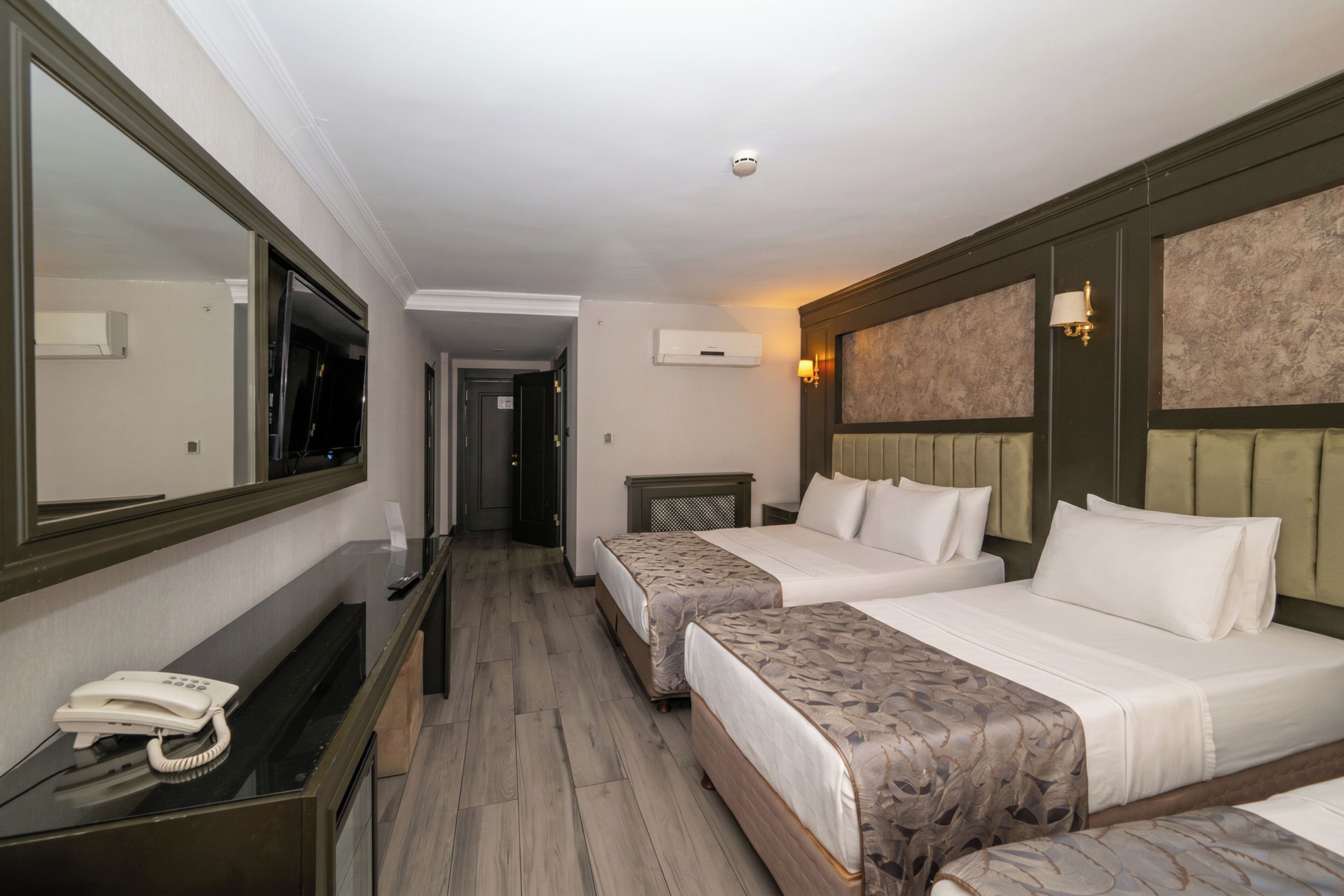 Habitación de hotel con dos camas, un escritorio y un teléfono, además de un espejo.