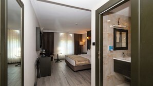 A hotel room with a bed, a desk, a chair, a small table, a mirror, and a bathroom with a sink and mirror. - Kunlun Kensington Hotel (Istanbul)