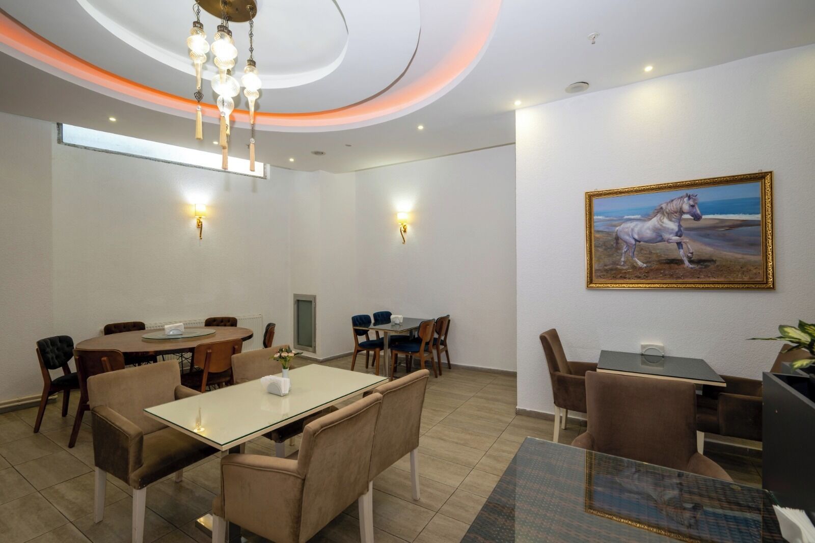 A hotel room with a dining area, a painting of a horse, and a chandelier.