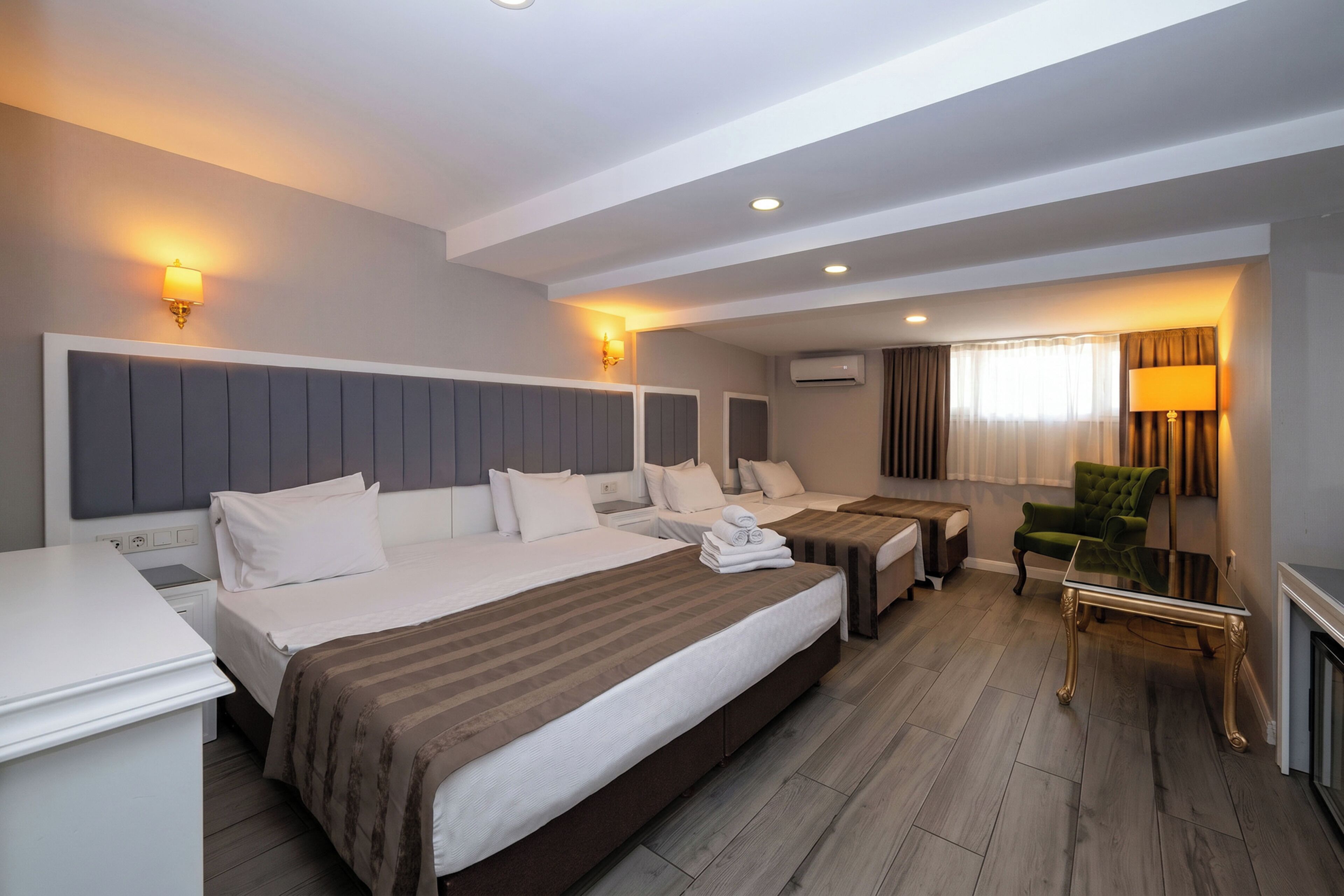 A hotel room with a large bed, two bedside tables, a green armchair, a glass coffee table, and a fireplace.