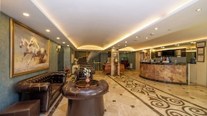 A lobby with a reception desk, a leather sofa, a coffee table, and a staircase leading to another floor. - Kunlun Kensington Hotel (Istanbul)
