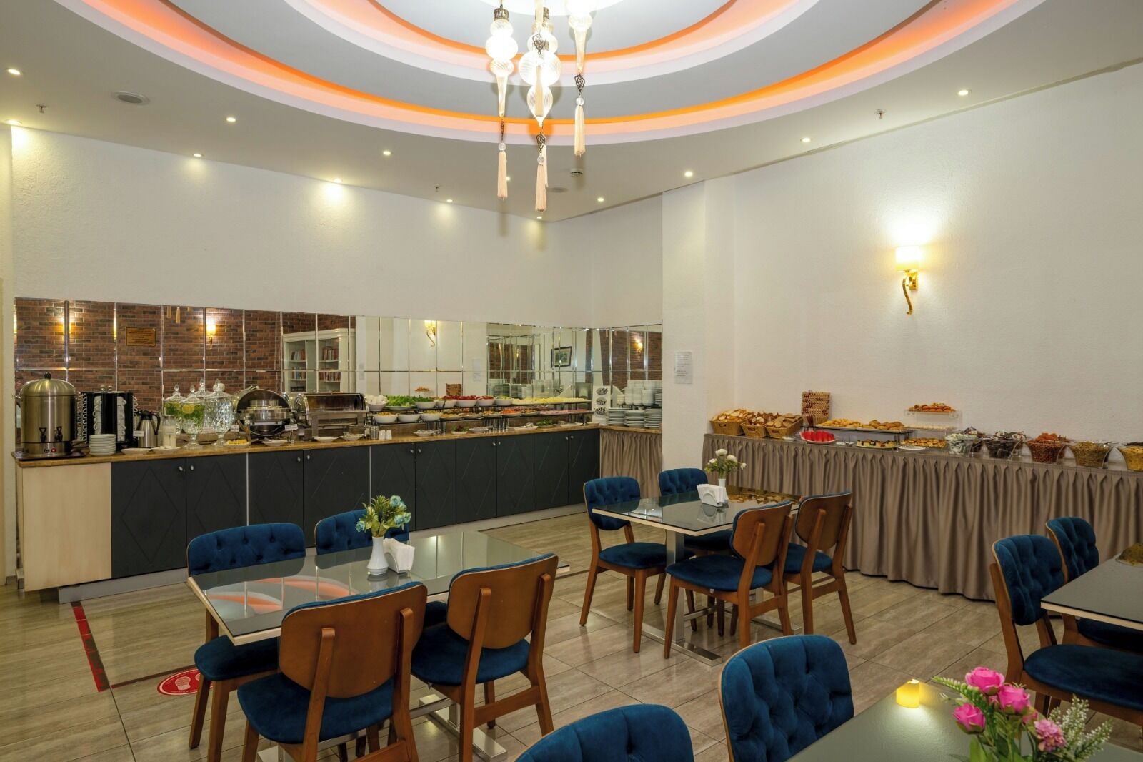 Un comedor con bufé, sillas tapizadas en azul, una araña y una cocina moderna al fondo.