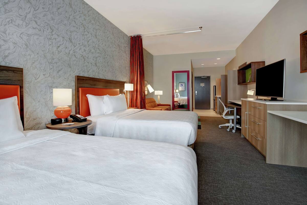 Une chambre d’hôtel avec deux lits, un bureau, une télévision et une salle de bain visible au fond.