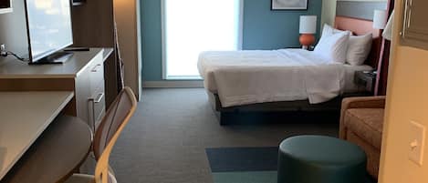A hotel room with a desk, chair, bed, and ottoman.