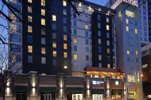 Un hôtel à plusieurs étages avec des fenêtres illuminées, une banque bien visible et un café Starbucks.