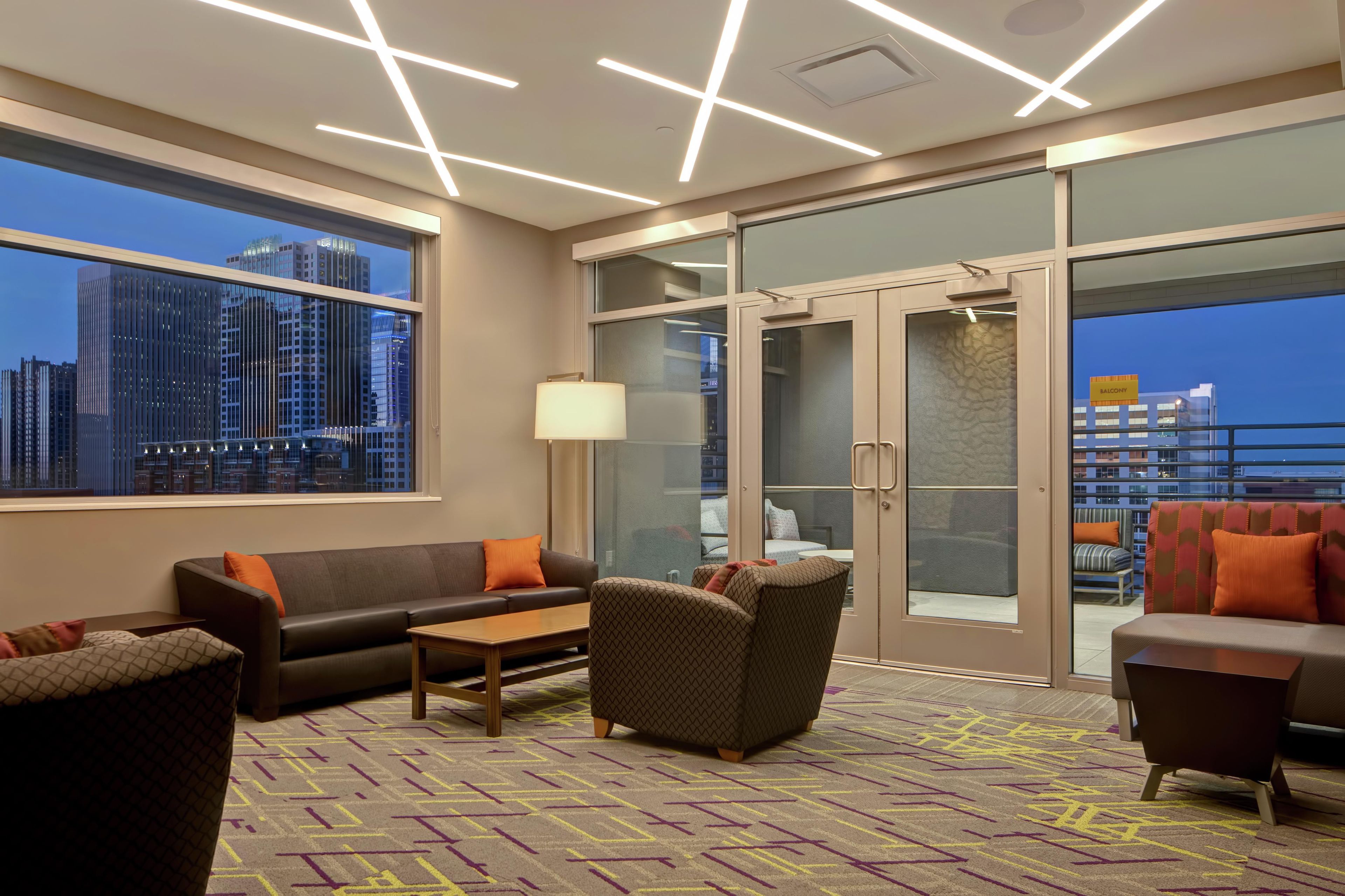 A modern hotel lobby with a sofa, armchairs, a coffee table, and a patterned carpet.