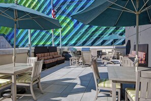 Un espace extérieur aménagé avec des tables et des chaises, des parasols et un mur décoré d’un motif particulier en arrière-plan.