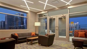 A modern hotel room with a city view, a balcony, and a seating area with a sofa and armchairs.