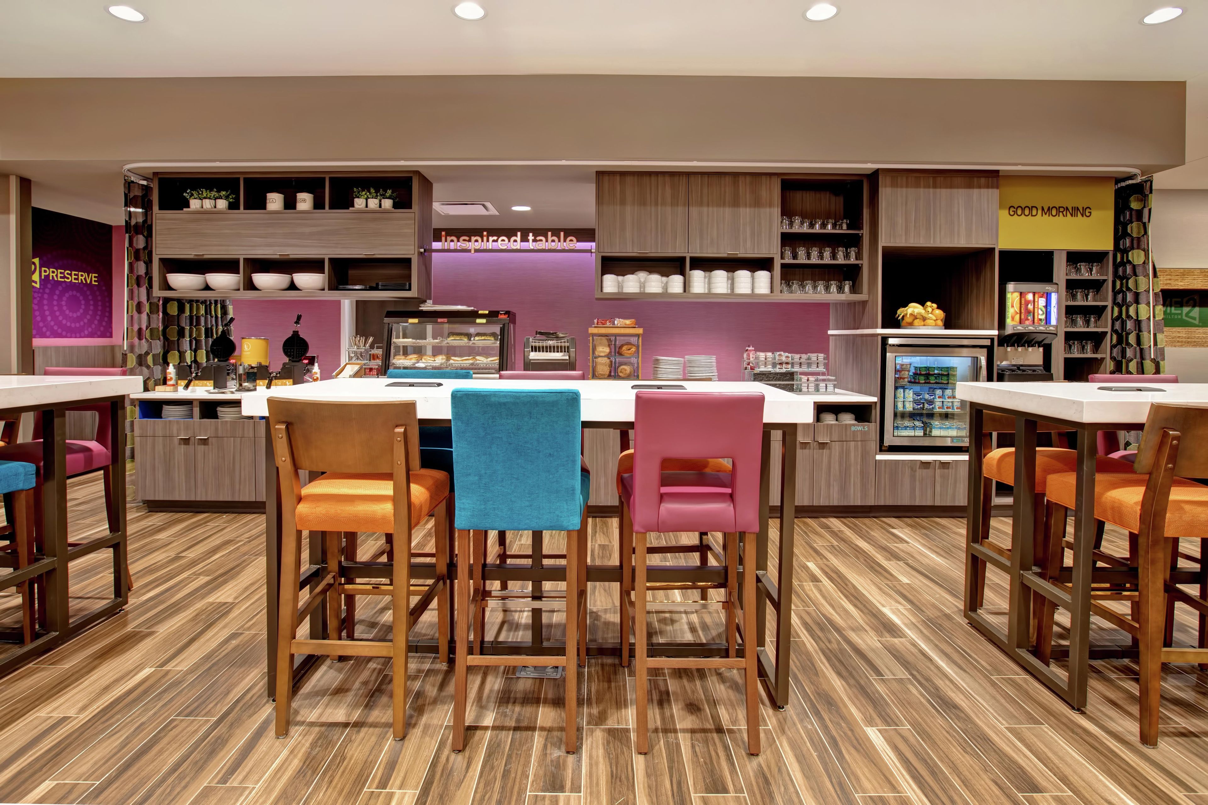 Un café moderno con una isla central, taburetes de bar y una variedad de utensilios de cocina en estantes.
