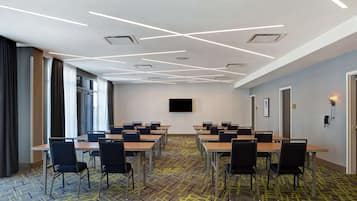 A conference room with a modern ceiling design, multiple tables, and chairs arranged for meetings.