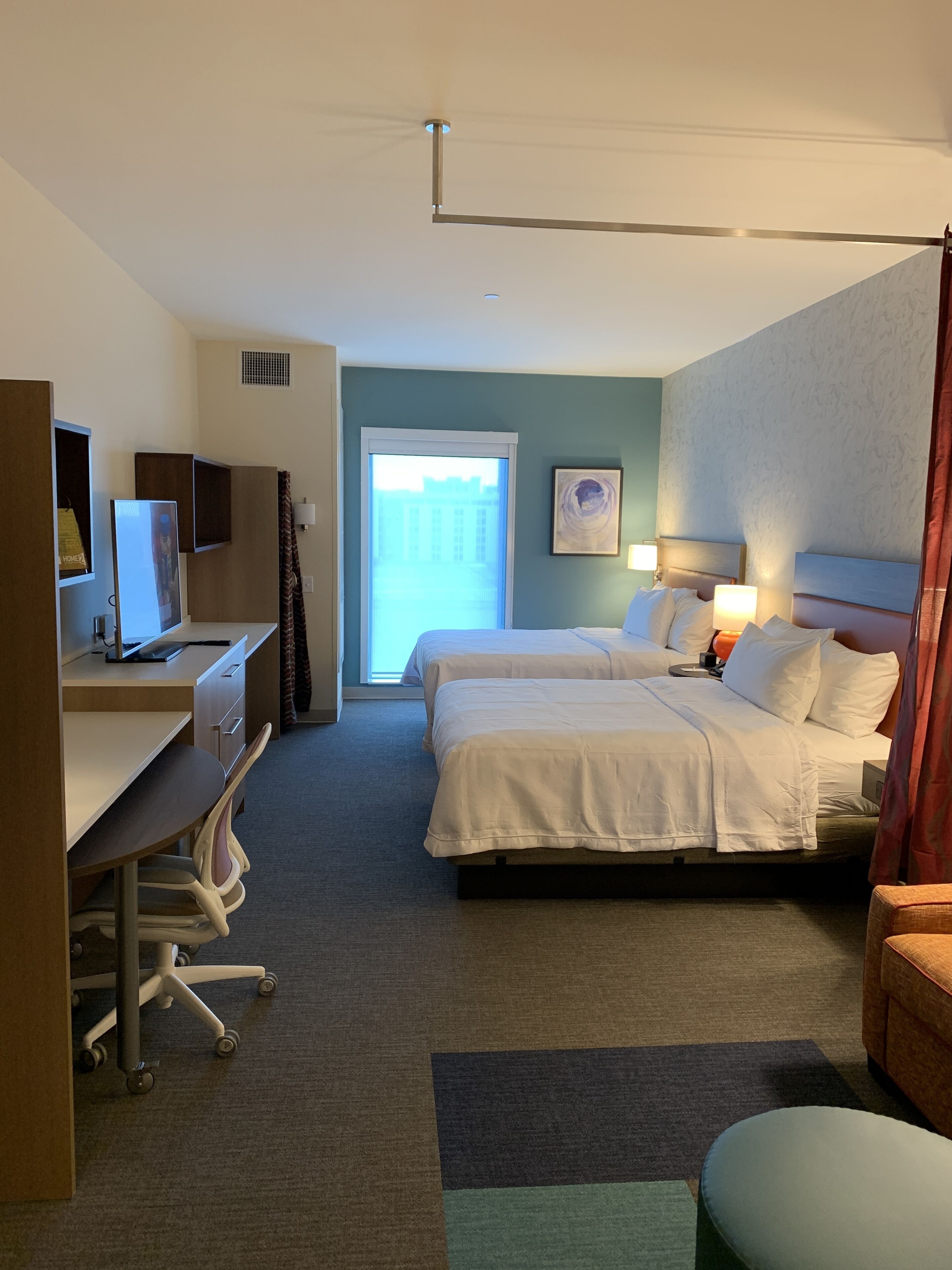 A hotel room with a desk, two beds, a window with a view, and a bathroom door.