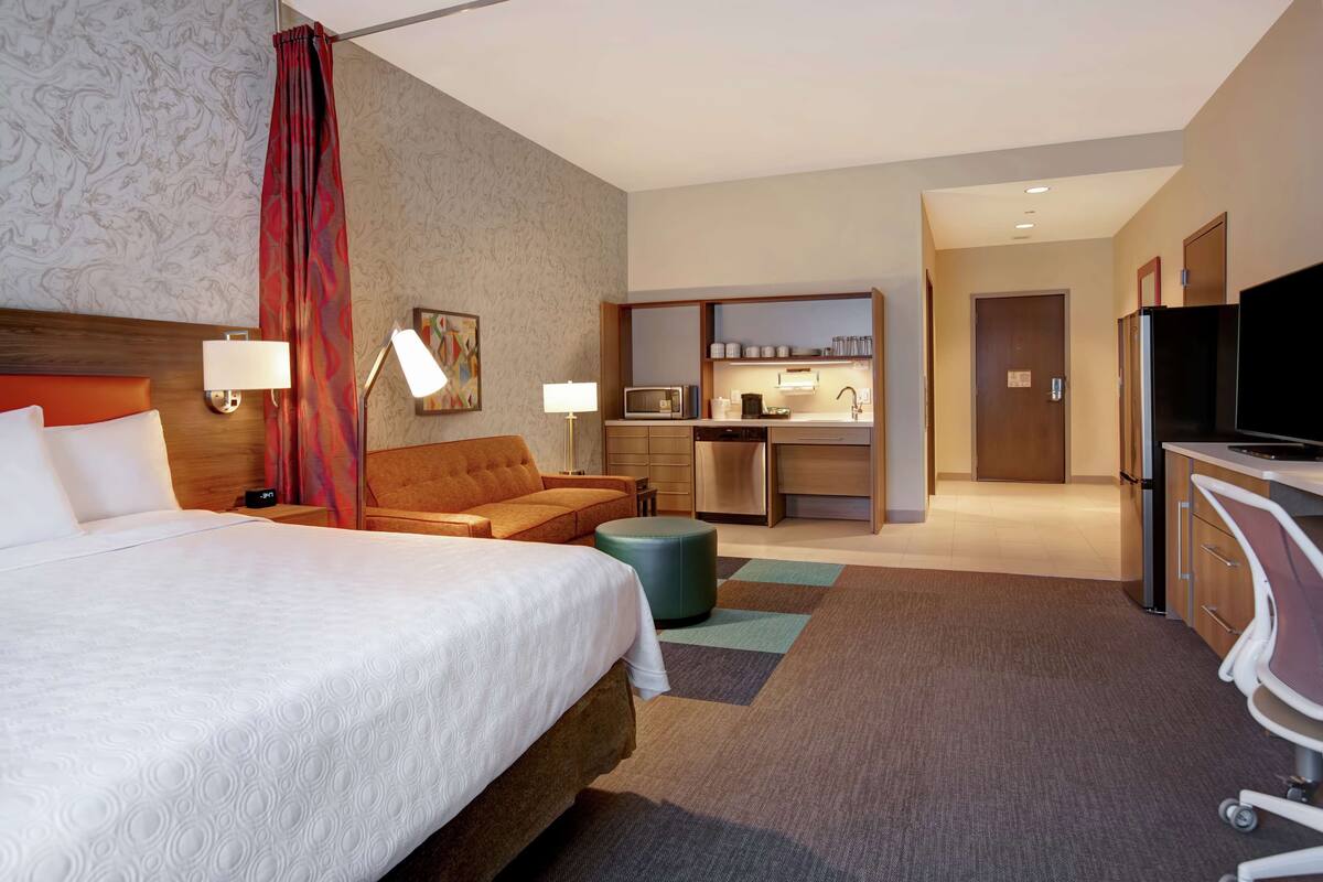 Une chambre d’hôtel équipée d’un lit, d’un canapé, d’un bureau, d’une télévision, d’un four à micro-ondes, d’un réfrigérateur et d’une kitchenette.
