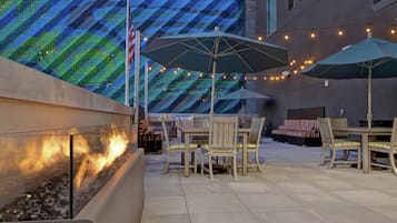 Une terrasse extérieure dotée d’un foyer, de tables, de chaises et de guirlandes lumineuses.