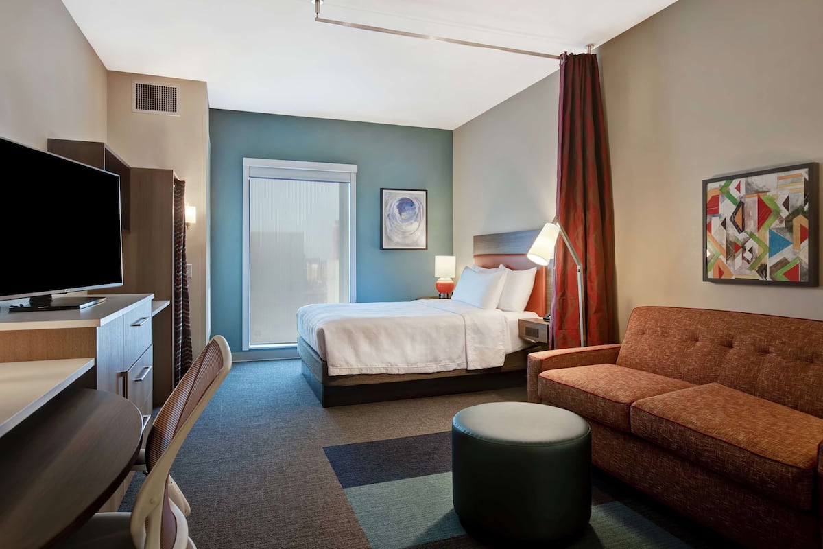 Une chambre d’hôtel avec un lit, un canapé, un bureau avec une télévision, une lampe et un tableau au mur.