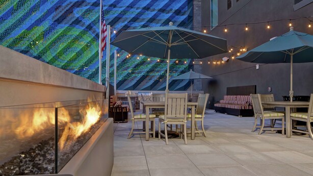 An outdoor patio with a fire feature, tables, chairs, and string lights.