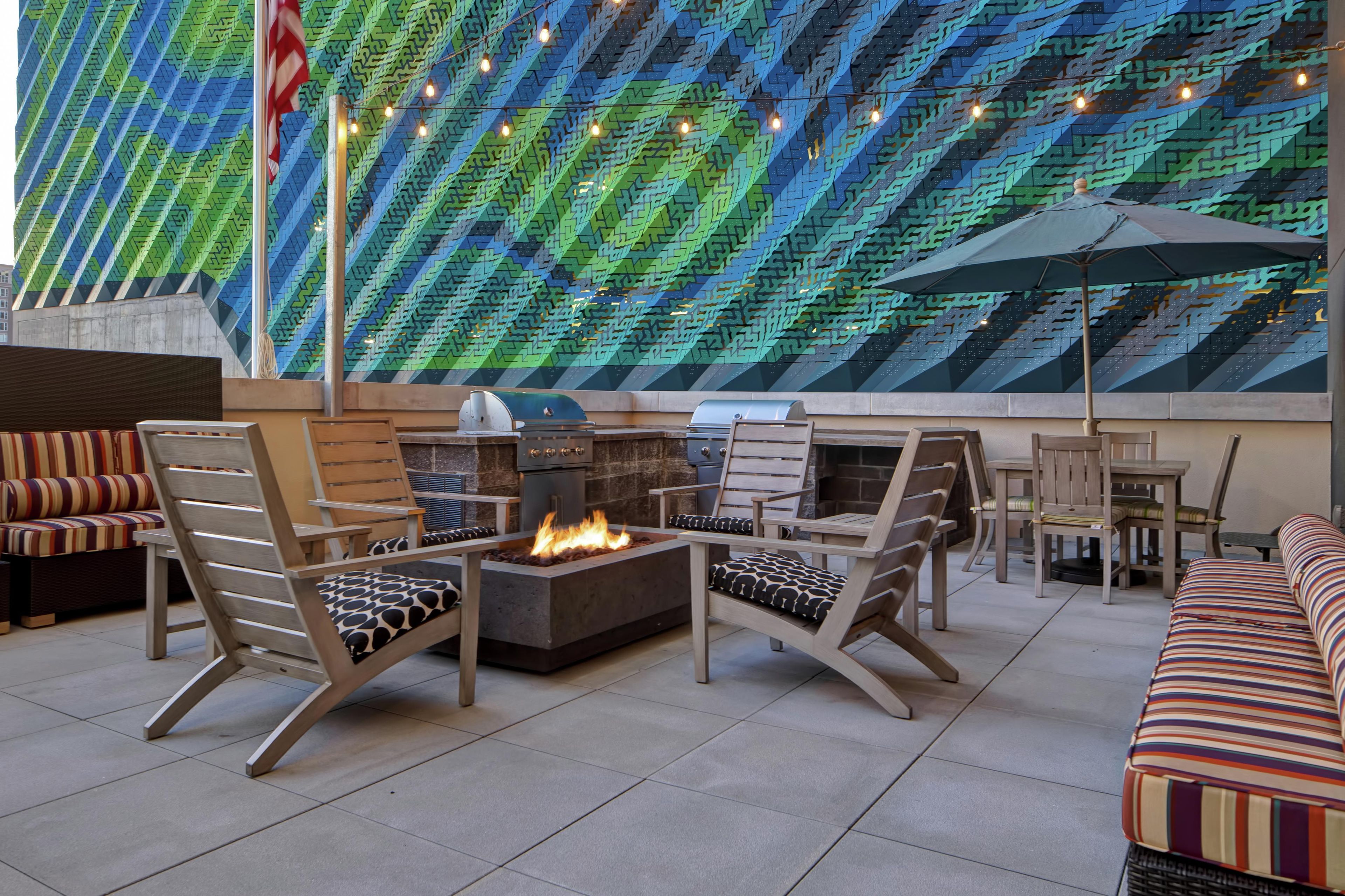 A modern outdoor seating area with fire pits, lounge chairs, and a patterned wall.