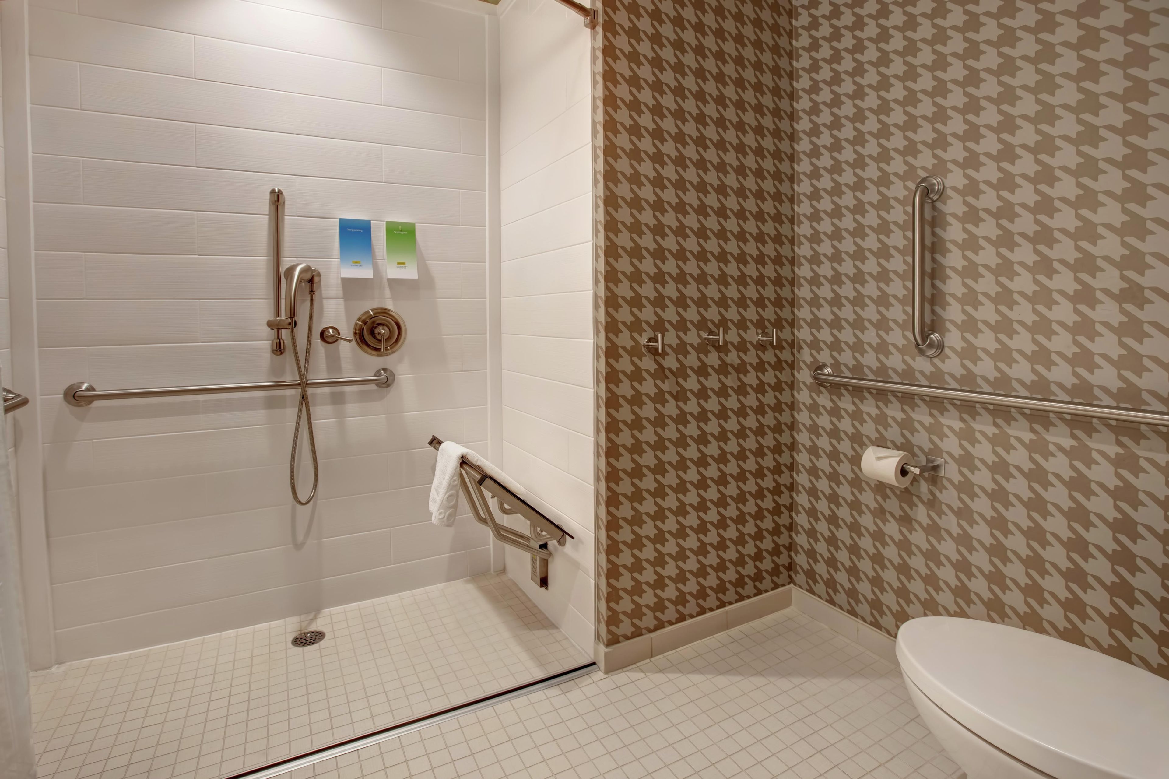 Een badkamer met een inloopdouche, handgrepen, toilet en een behang met patroon.