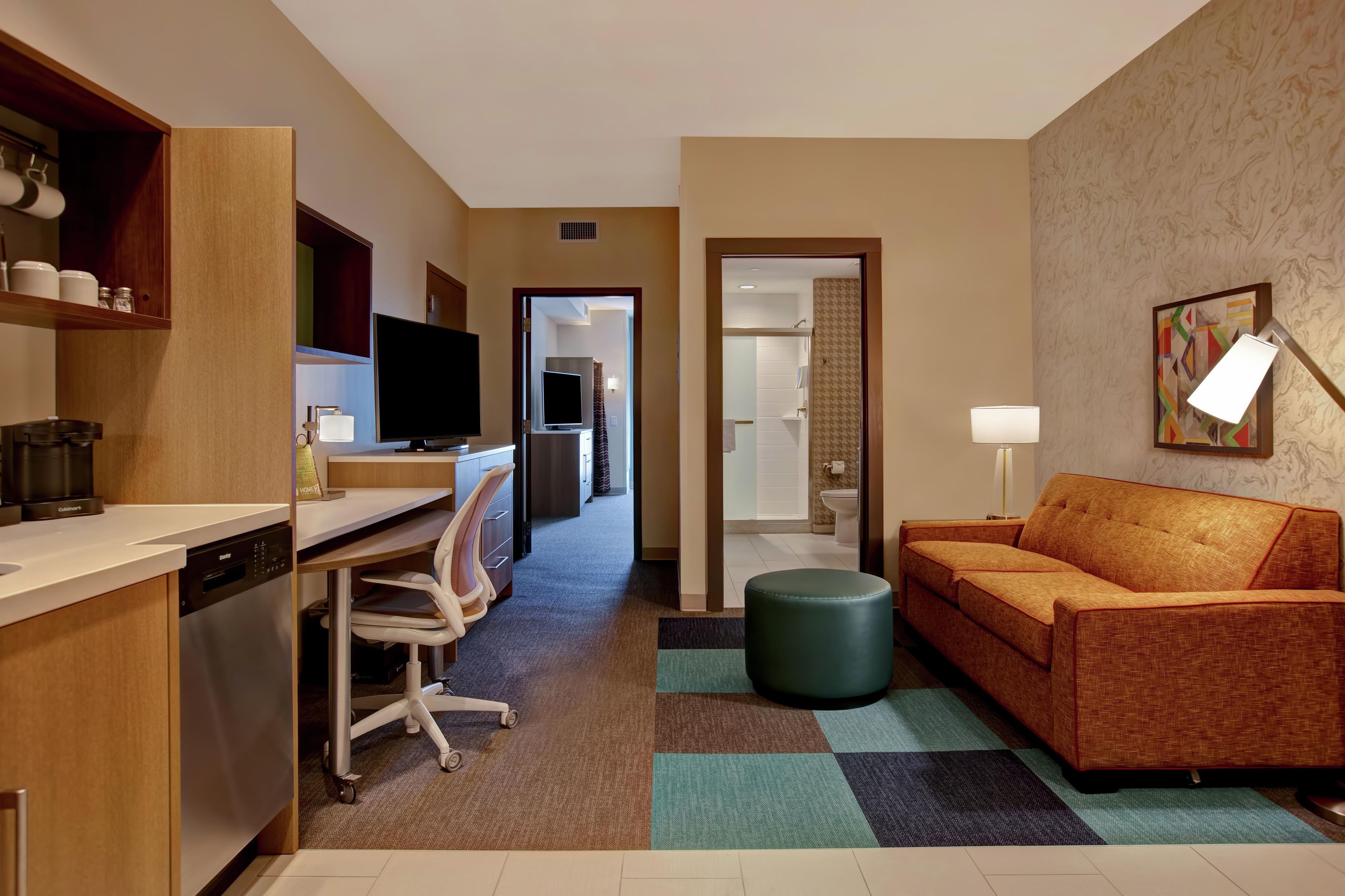 Een hotelkamer met een kitchenette, een bank, een televisie en een zichtbare badkamer door een geopende deur.