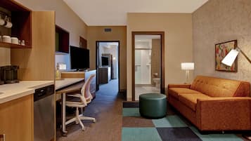 Een hotelkamer met een kitchenette, een bank, een televisie en een zichtbare badkamer door een geopende deur.