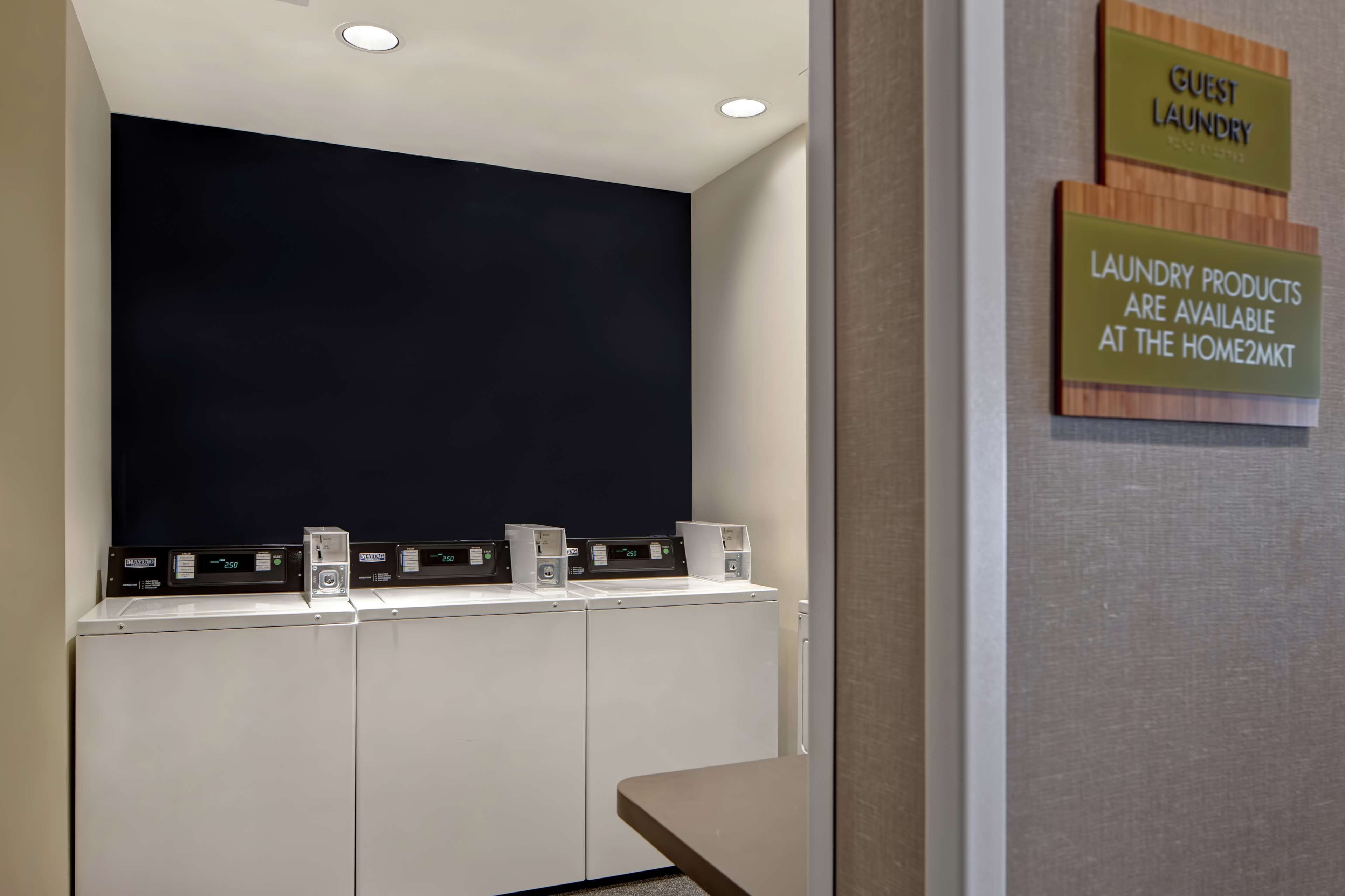 A laundry area with signs indicating guest laundry and available products at the Home2MKT.