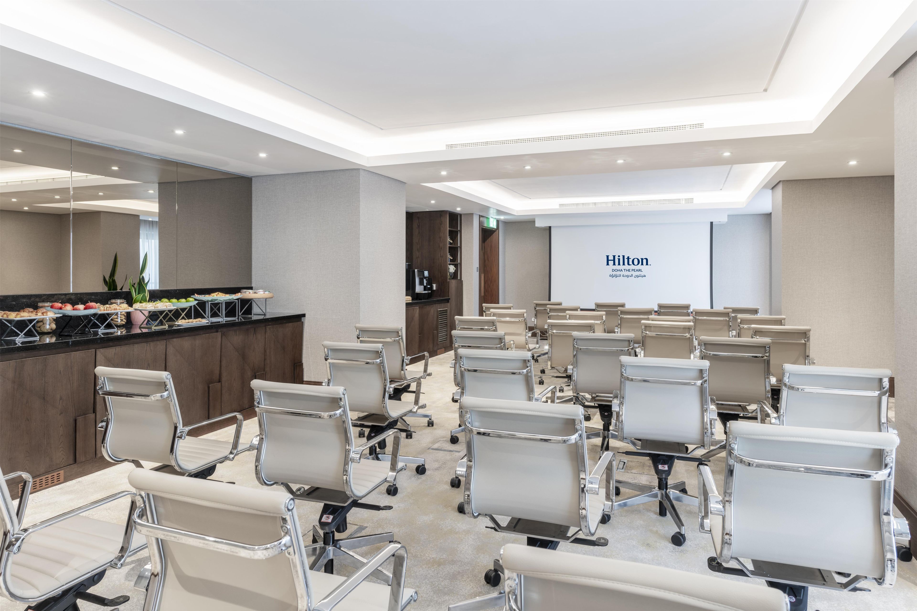 Una sala de conferencias con filas de sillas de oficina, una mesa de recepción con estación de café y una gran pared con el logotipo de Hilton.