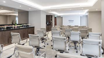 Una sala de conferencias con filas de sillas de oficina, una mesa de recepción con estación de café y una gran pared con el logotipo de Hilton.