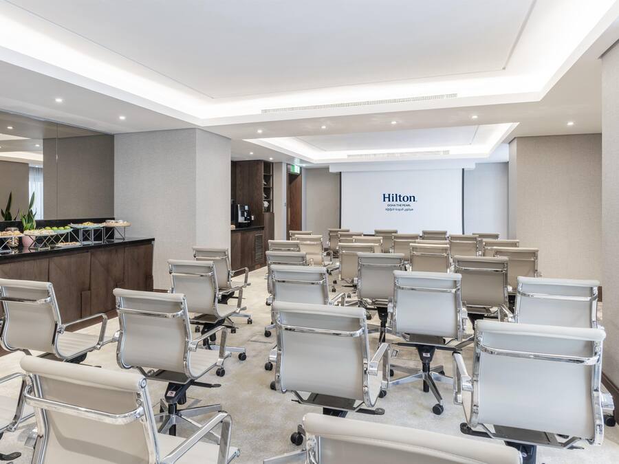 Una sala de conferencias con filas de sillas de oficina, una mesa de recepción con estación de café y una gran pared con el logotipo de Hilton.
