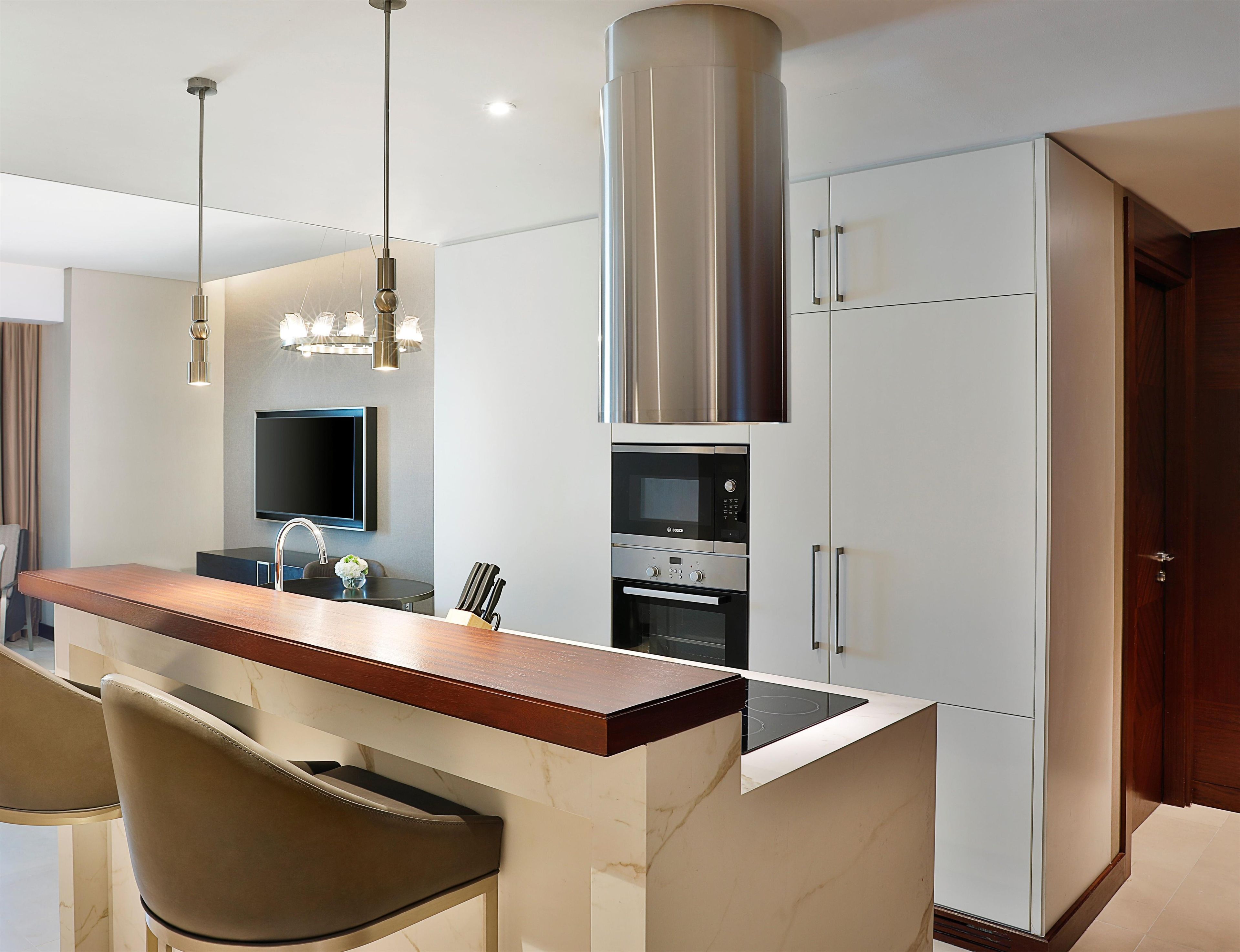 A modern kitchen with a central island, stainless steel appliances, and a flat-screen TV mounted on the wall.