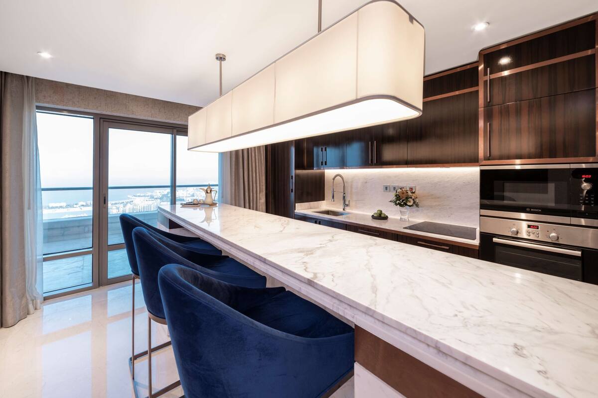 Une cuisine moderne dotée d’un plan de travail en marbre, de meubles en bois foncé, d’une grande fenêtre et d’une vue sur la ville.